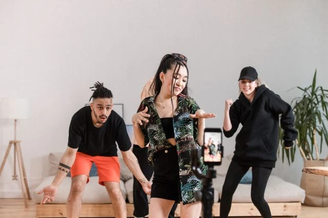 Creators Recording a TikTok Dance Video Three young creators performing a synchronized dance routine in front of a smartphone mounted on a tripod.